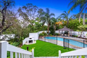 una piscina al aire libre con una valla blanca y césped verde en 4 Bedroom Family Home with Pool - Uplands Drive - Q Stay en Gold Coast