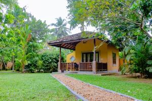 a yellow house with a porch in a garden at Birds Paradise Cabanas Unawatuna in Unawatuna