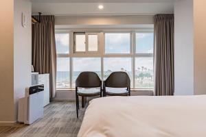 une chambre d'hôtel avec un lit et deux chaises devant une fenêtre dans l'établissement Cocoon Hotel, à Jeju