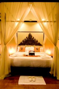 a bedroom with a bed with curtains and two shoes on it at Kanok Buri Resort in Lipa Noi