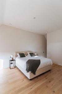 a white bedroom with a large bed and a wooden floor at Duisbeke Logies in Oudenaarde