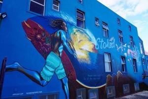 a mural of a woman holding a surfboard on a building at Beachside Studio Apartment on Surfers Corner in Cape Town +3 photos