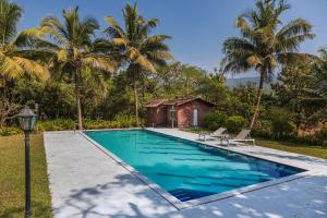 a swimming pool in front of a house with palm trees at SaffronStays Alma Grove, Kashid in Kashid