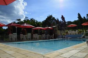 a swimming pool with tables and chairs and umbrellas at Pousada das Rosas in Miguel Pereira