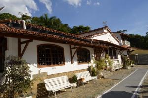 um edifício com dois bancos brancos à sua frente em Pousada das Rosas em Miguel Pereira