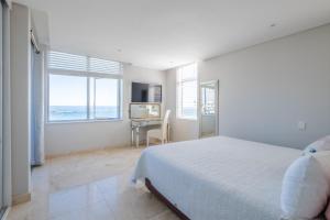 a white bedroom with a bed and a desk and windows at Beach Vista by Totalstay in Cape Town