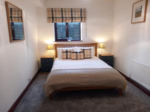 a bedroom with a bed with two night stands and two windows at Hayfellside Nook in Kendal