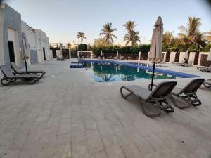 a swimming pool with two chairs and an umbrella at Hawana Salalah Laguna Studio in Salalah