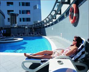 ROYAL CONCORDE HOTEL&SUITE في دبي: وجود امرأة جالسة على كرسي بجانب مسبح