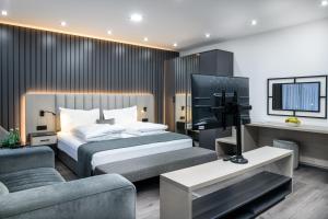 ein Schlafzimmer mit einem Bett, einem TV und einem Sofa in der Unterkunft PARKHOTEL BRAUNAU - 24 Stunden Self Check-IN in Braunau am Inn