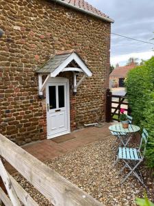 a brick house with a white door and a table and chairs at Curlew Cottage in Sedgeford