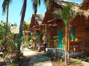 a man standing outside of a wooden house with palm trees at Green Garden Homestay in Can Tho