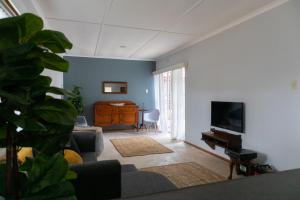 a living room with a tv and a couch and a table at The Jbaynian Guesthouse in Jeffreys Bay