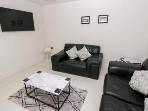 a living room with a black leather couch and a table at LunaRoxx, 6 Meadow Gardens, Kilgetty in Kilgetty