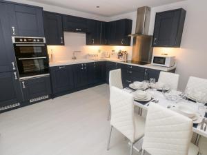 a kitchen with black cabinets and a table with white chairs at LunaRoxx, 6 Meadow Gardens, Kilgetty in Kilgetty