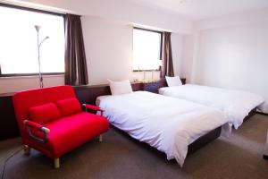 Green Rich Hotel Oita Miyakomachi في أويتا: غرفة فندقية بسريرين وكرسي احمر