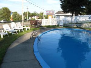 uma grande piscina com cadeiras e cadeiras brancas em Motel Clair Mont em Sainte-Agathe-des-Monts