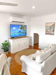 een woonkamer met witte banken en een flatscreen-tv bij Lammermoor Lodge Holiday Home Yeppoon in Yeppoon