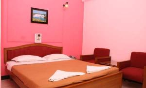 a pink bedroom with a bed and a red chair at Margao Residency in Madgaon