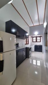 une grande cuisine avec des armoires noires et un réfrigérateur blanc dans l'établissement Family Tides Guest, à Kochchikade