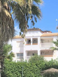 a white building with palm trees in front of it at Beautiful 2 Bed Apartment on Villamartin Plaza in Villacosta