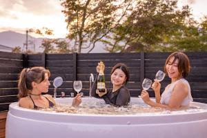 3 femmes assises dans un bain à remous tenant des verres à vin dans l'établissement IZA近江舞子, à Minami-komatsu