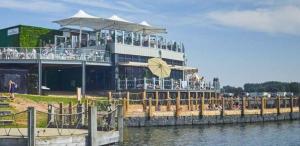 a building with people sitting on a pier next to the water at The Wardens Hideaway - Tattershall Lakes Country Park in Tattershall