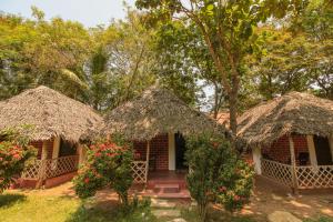 dwa małe domki z dachem krytym strzechą w lesie w obiekcie Prince Park w mieście Puducherry