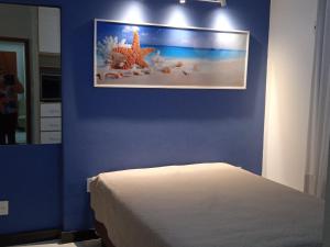 a bedroom with a blue wall with a bed and a picture at 100 metros da praia das Castanheiras,com garagem, internet, cadeiras de praia, cooler,roupas de cama e banho in Guarapari