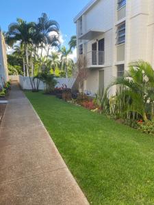 Pearlridge Gardens and Tower Aiea, Hawaii 96701 في Aiea: ساحة عشبية بجوار مبنى به أشجار نخيل