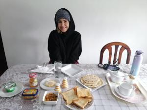 Una mujer sentada en una mesa con comida. en Nuwara eliya mountain view homestay, en Nuwara Eliya