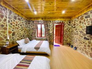 a bedroom with two beds and a stone wall at Lan Rừng Homestay in Lũng Niêo