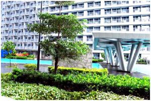 ein großes weißes Gebäude mit einem Baum davor in der Unterkunft Iona Reign's Vacation Unit at FAME Residences in Manila
