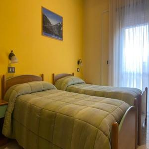 two beds in a room with yellow walls at Hotel Giampy in Assergi