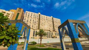 een groot wit gebouw met blauwe pilaren ervoor bij فندق مسك ام القرى Misk Umm Al Qura Hotel in Mekka