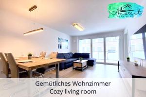 a living room with a table and a blue couch at Auszeit Apartment SMILE am Uferpark - nur 100 m bis zum Bodensee, direkt am Bodenseeradweg, 2 Schlafzimmer, 2 Sonnenbalkone, schnelles WLAN, kostenloser Tiefgaragenstellplatz, für bis zu 4 Personen in Friedrichshafen