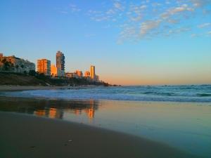 a beach with buildings and the ocean at sunset at Luxury Aparment 5 room 2 minutes from the beach in Bat Yam