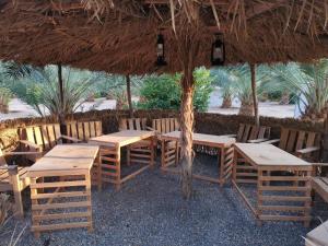 a restaurant with wooden tables and chairs under a straw umbrella at Almazham camp resort in AlUla
