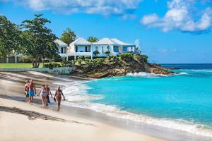 a group of people walking on the beach in front of a house at Hawksbill Resort Antigua - All Inclusive in Five Islands Village