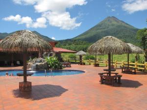 a resort with a pool with tables and straw umbrellas at Hotel La Pradera del Arenal in Fortuna