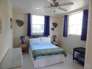 1 dormitorio con 1 cama con cortinas azules y ventilador de techo en Heywoods Villa en Saint Peter