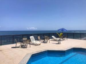 um pátio com uma piscina, mesas e cadeiras em Flat vista mar com estacionamento incluído em Salvador