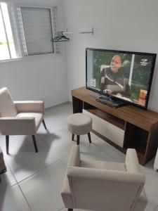 ein Wohnzimmer mit einem Flachbild-TV und Stühlen in der Unterkunft Apto a 300 metros da Canção Nova. Condomínio da Fé in Cachoeira Paulista