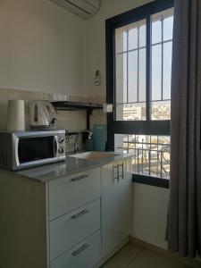 eine Küche mit einer Spüle, einer Mikrowelle und einem Fenster in der Unterkunft נופש מול הכנרת Vacation in front of the Sea Galilee in Tiberias