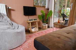 uma sala de estar com uma cama e uma televisão de ecrã plano em Tiny House Hilver - uniek en sfeervol huisje middenin het bos em Diessen