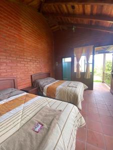 3 camas en una habitación con una pared de ladrillo en Hospedaje Pondoa - Baños de Agua en Baños