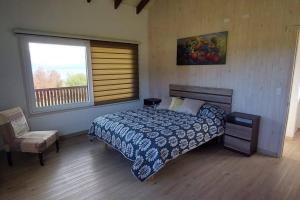 a bedroom with a bed and a chair and a window at Cabaña frente al Lago Llanquihue in Llanquihue