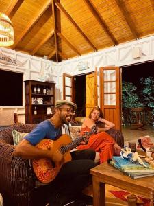 Ein Mann und eine Frau sitzen auf einer Couch und spielen Gitarre in der Unterkunft The Palms - Caribbean Paradise in Playa Aguadulce