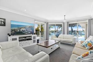 a living room with white furniture and a flat screen tv at Voyagers Resort - Stunning home! in Banksia Beach
