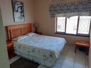 a bedroom with a bed with a blue comforter and two windows at Uvongo square Unit 24 in Uvongo Beach